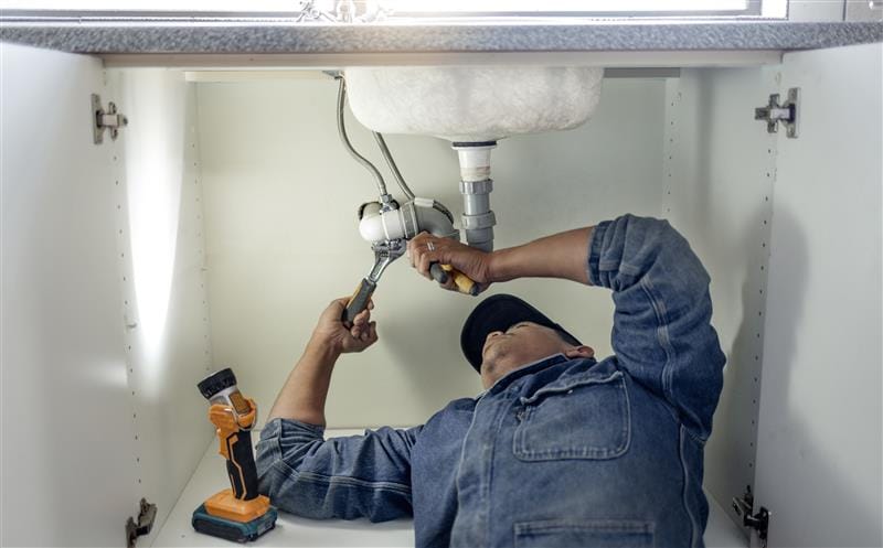 Plumber repairing pipes beneath a bathroom sink in Fort Pierce
