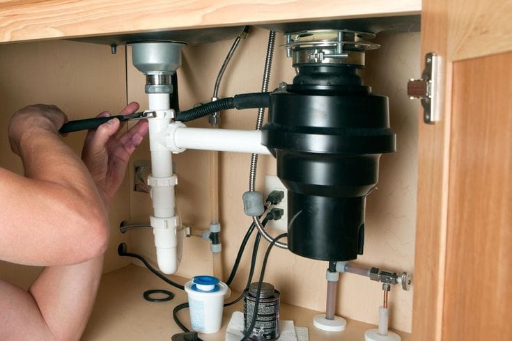 Plumber installing a garbage disposal beneath a kitchen sink in Fort Pierce