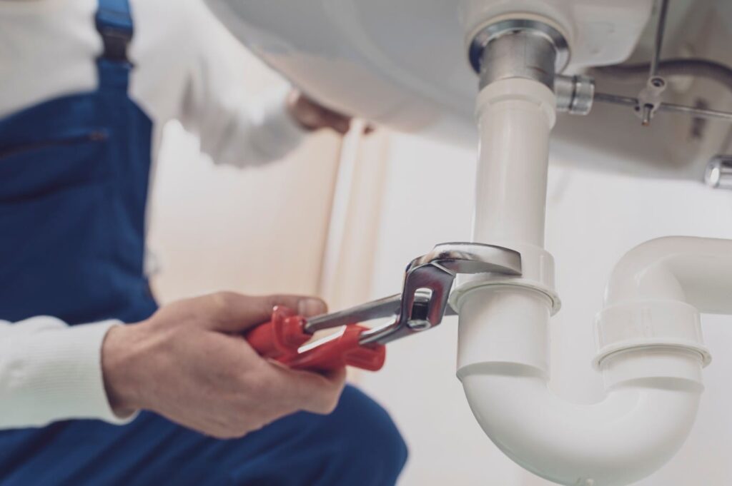 Plumber repairing a white drain pipe beneath a sink in Fort Pierce