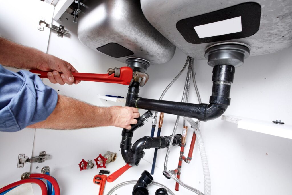Plumber repairing drain pipes beneath a kitchen sink in Fort Pierce